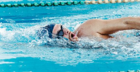 Hombre con gorro azul y gafas de natación nadando en una calle de piscina olímpica.