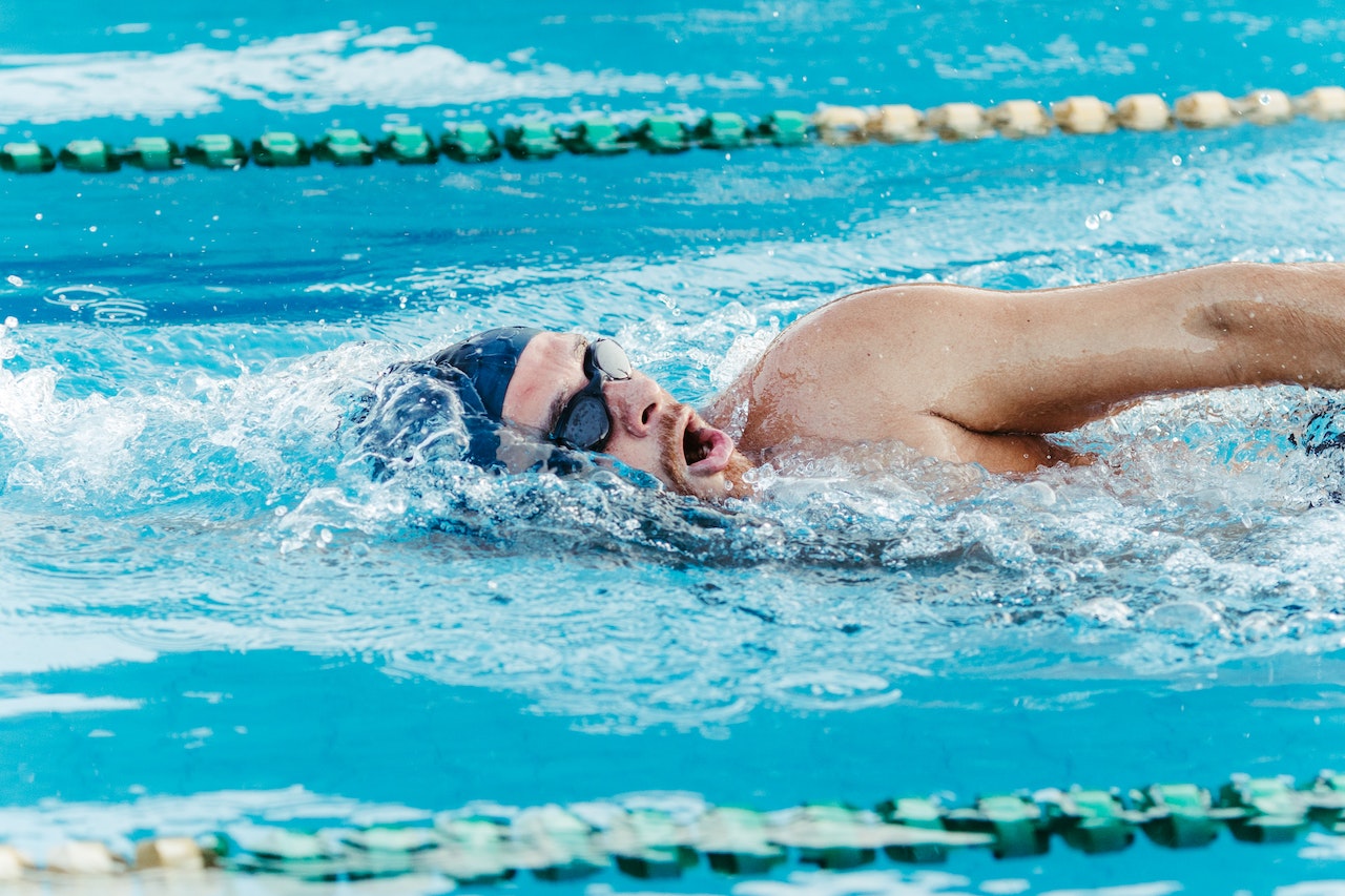 Hombre con gorro azul y gafas de natación nadando en una calle de piscina olímpica.